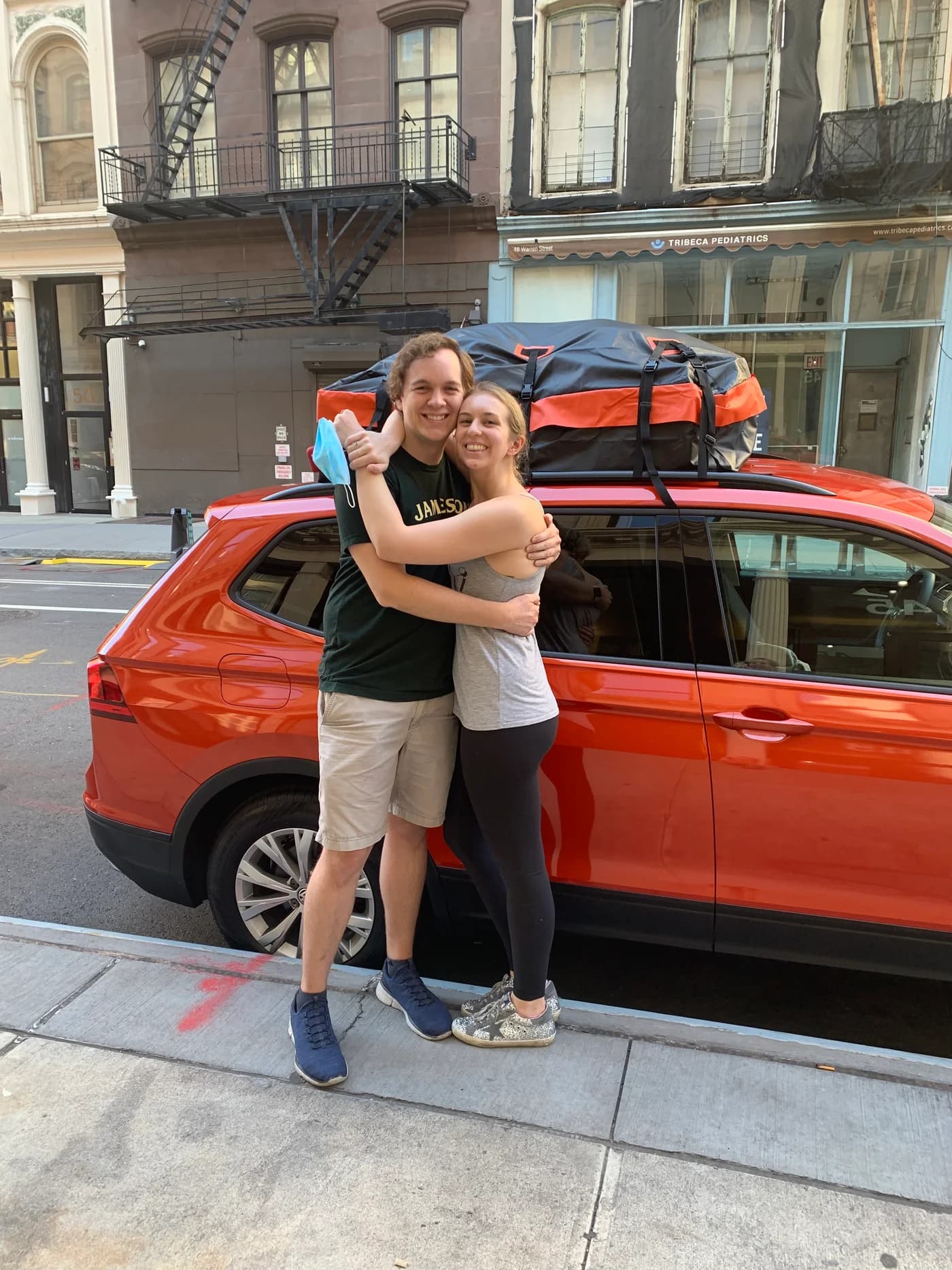Jay and Gabi hugging beside a packed orange car.